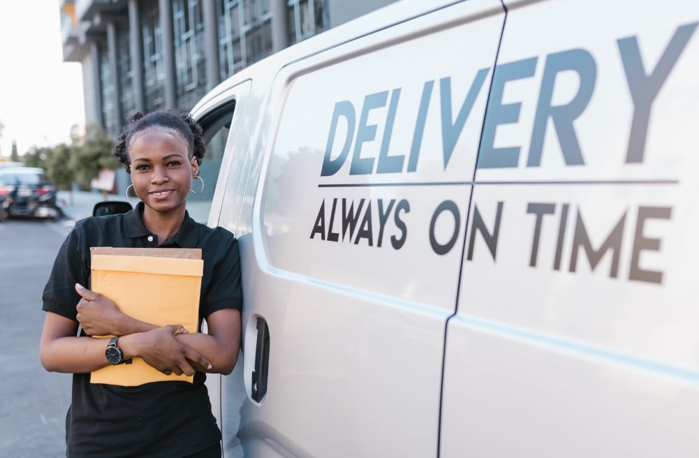 Smiling courier holding a parcel envelope beside a delivery van